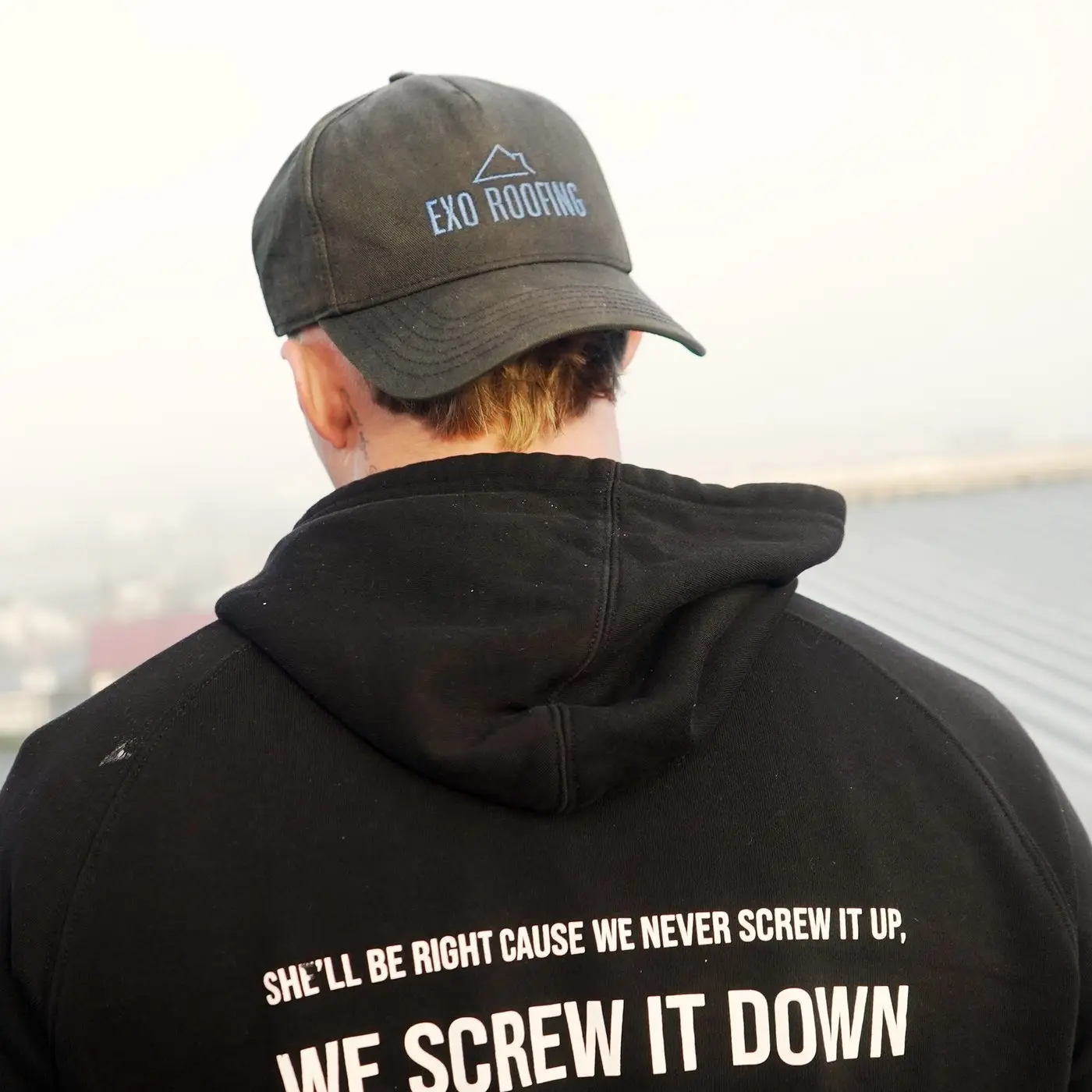 An Exo Roofing crew hoodie reading "She'll be right cause we never screw it up — we screw it down"